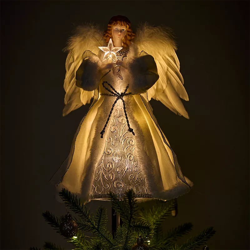 A lighted angel tree topper on top of the Christmas tree in the dark