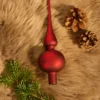 There is a red matte glass spherical finial Christmas tree topper, branches and two pine cones on the carpet