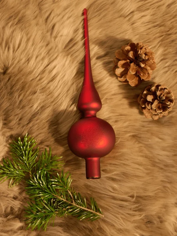 There is a red matte glass spherical finial Christmas tree topper, branches and two pine cones on the carpet