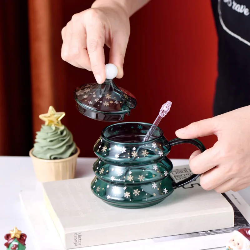 A man holds the Christmas tree wine glass coffee mug with lid and straw spoon on the table