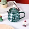 There is a Christmas tree wine glass coffee mug with lid and straw spoon on the table