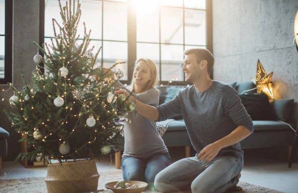 A man and woman are decorating their miniature Christmas tree