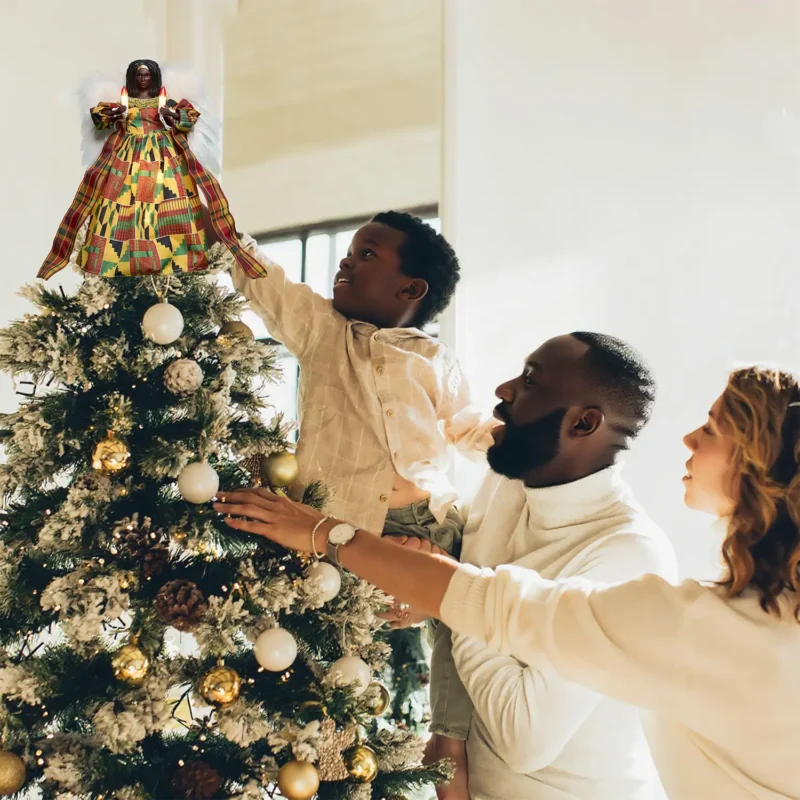 Heartwarming Christmas moment: father helps boy put a kente black angel tree topper while mother looks on smiling
