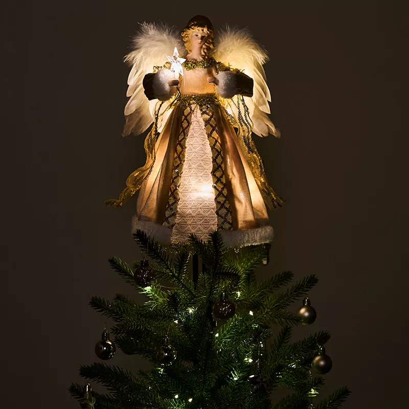 A gold animated angel tree topper in the dark on a Christmas tree