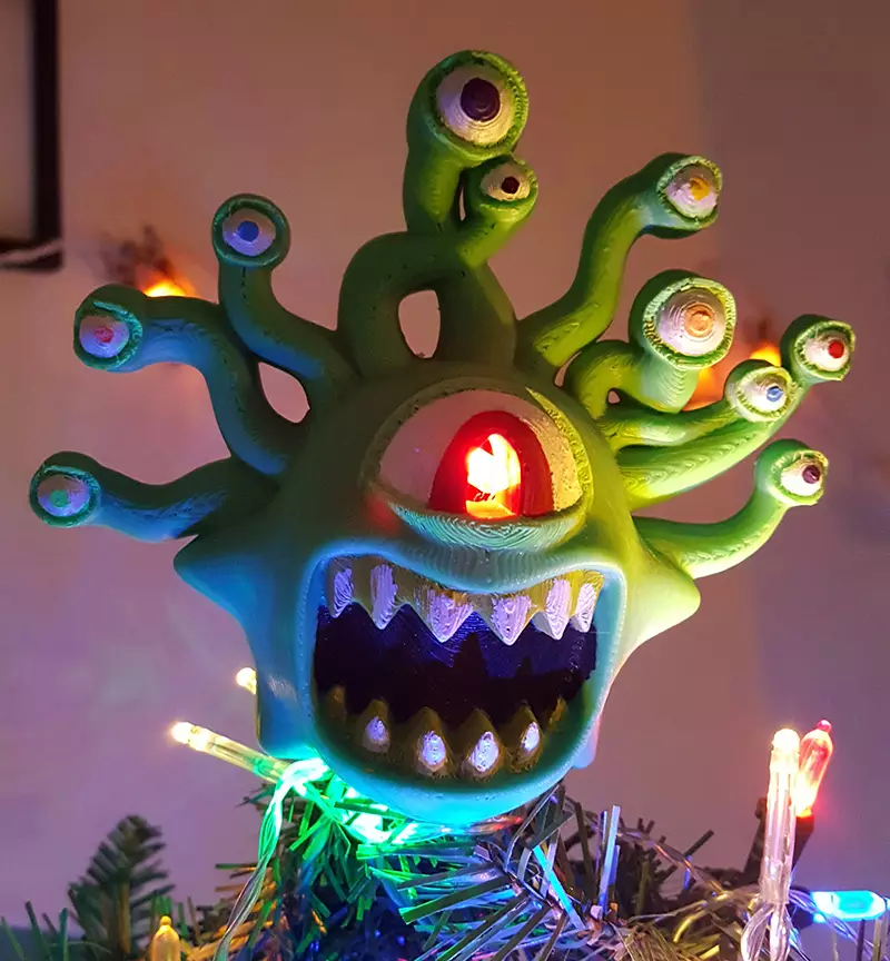 A green biblically beholder tree topper​ on top of a Christmas tree