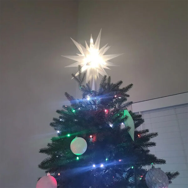 There is a warm white lighted Moravian star tree topper on a Christmas tree