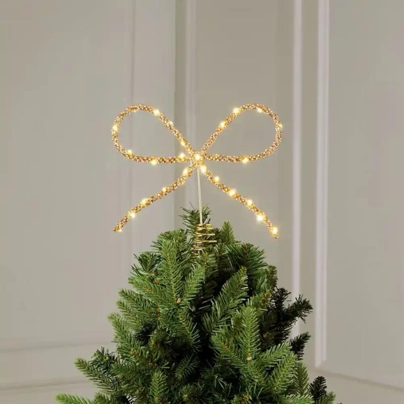 A lighted rhinestone bow tree topper stands on the tree.